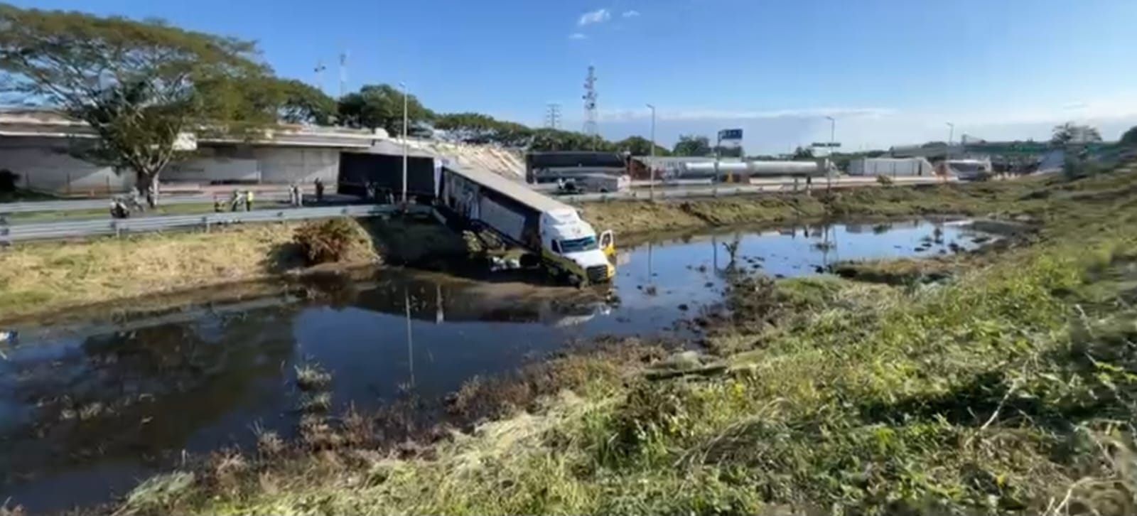 Tráiler cargado de cervezas brinca la valla y cae a laguna